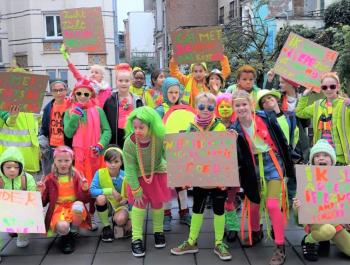 Schüler der Grundschule De Kleine Stad posieren mit bunten Kleidern und Pappschildern mit Slogans für gesündere Luft und nachhaltige Mobilität.