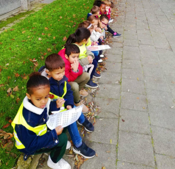 Die Kleinkinder von Het Pieterke sitzen mit Blättern in den Händen auf dem Bürgersteig. Sie zählen den Verkehr.